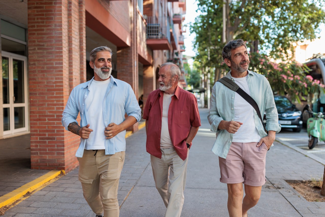 Three men smiling and walking together along an urban street