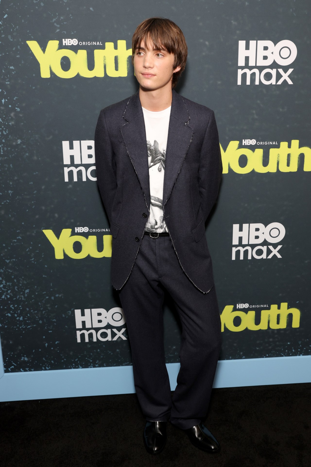 Aran Murphy in a dark blazer and graphic T-shirt posing at the HBO Youth premiere backdrop in New York City.
