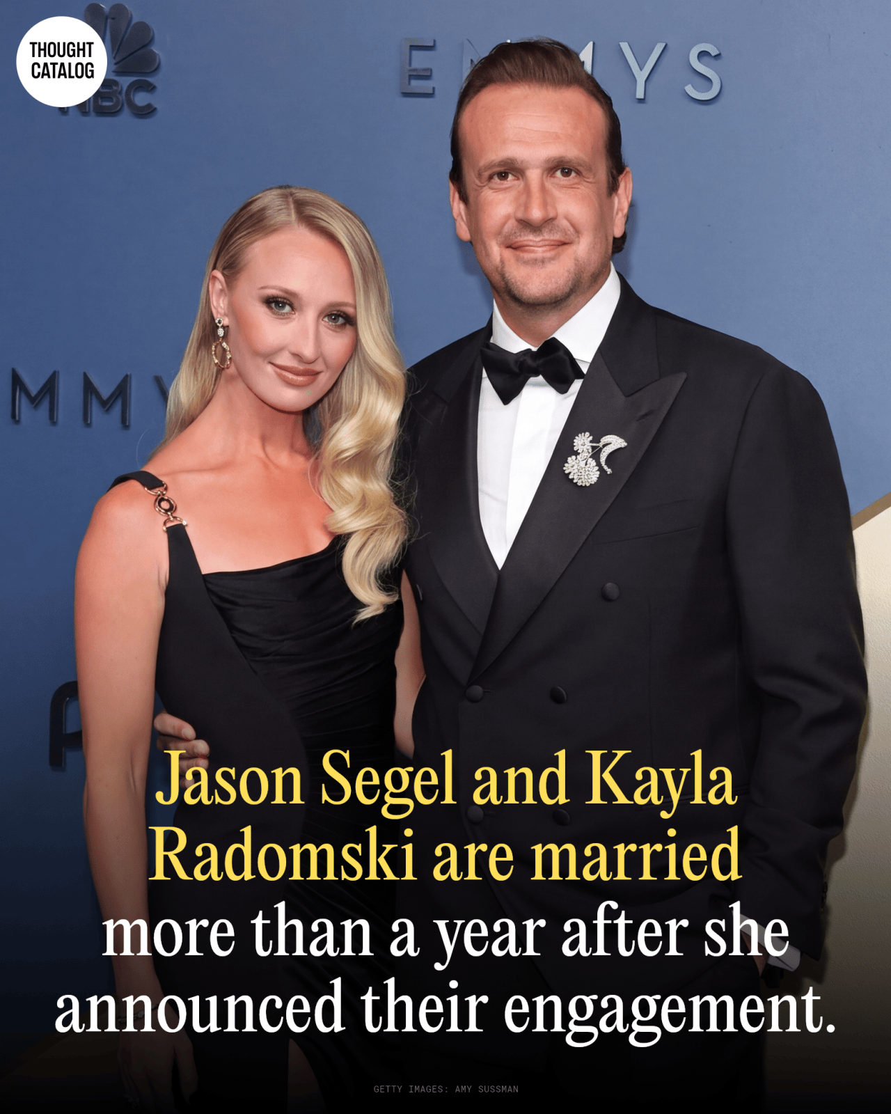Jason Segel in a black tuxedo with brooch and Kayla Radomski in a black gown posing together at the Emmy Awards.