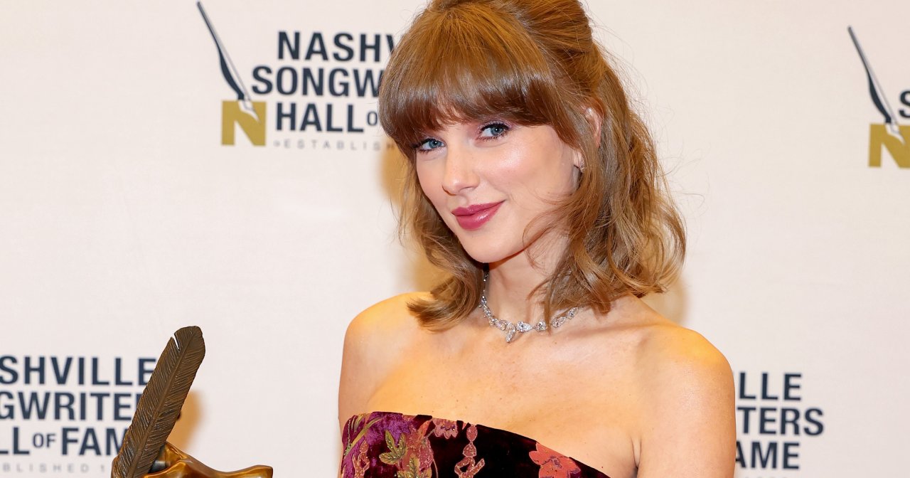 Woman in a floral velvet strapless mini dress holding a bronze Nashville Songwriters Hall of Fame award, posing in front of a Hall of Fame step-and-repeat banner.