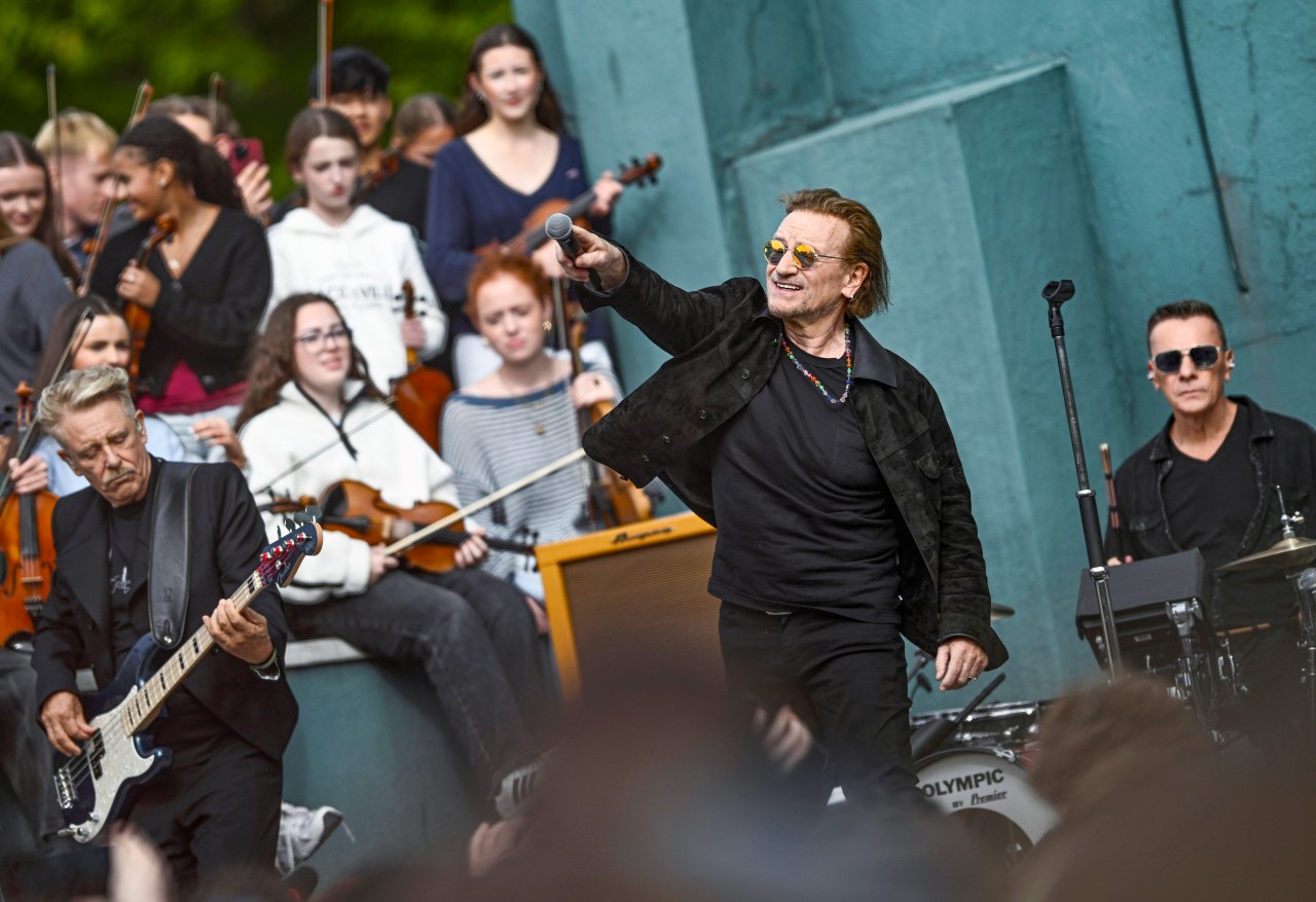 Adam Clayton, Bono, and Larry Mullen Jr. of U2 performing on stage at Mount Temple Comprehensive School in Dublin, Ireland